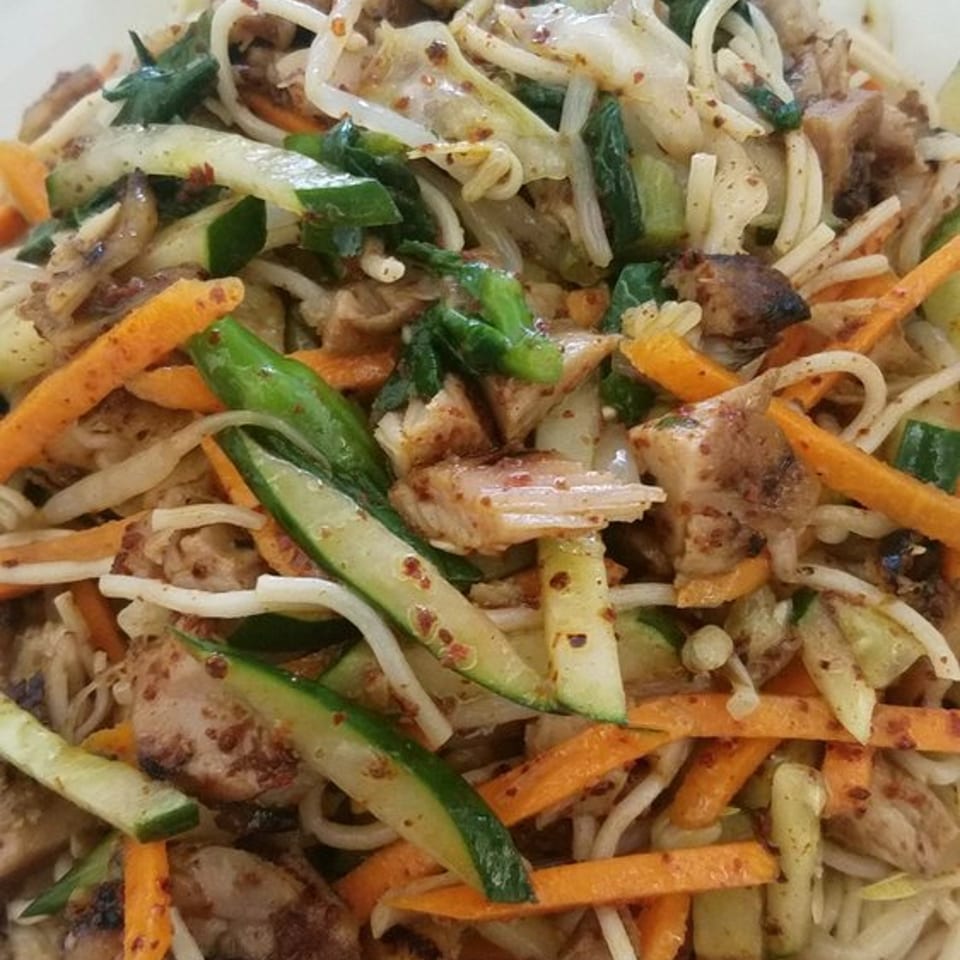 Close-up of Korean japchae noodles with chicken, carrots, zucchini, and cabbage.
