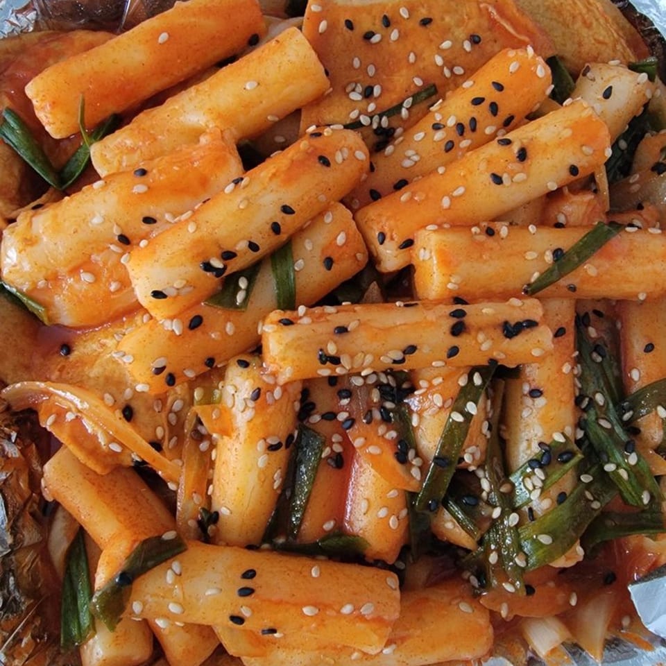 Close-up of Korean tteokbokki rice cakes with green onions and sesame seeds in a spicy sauce.
